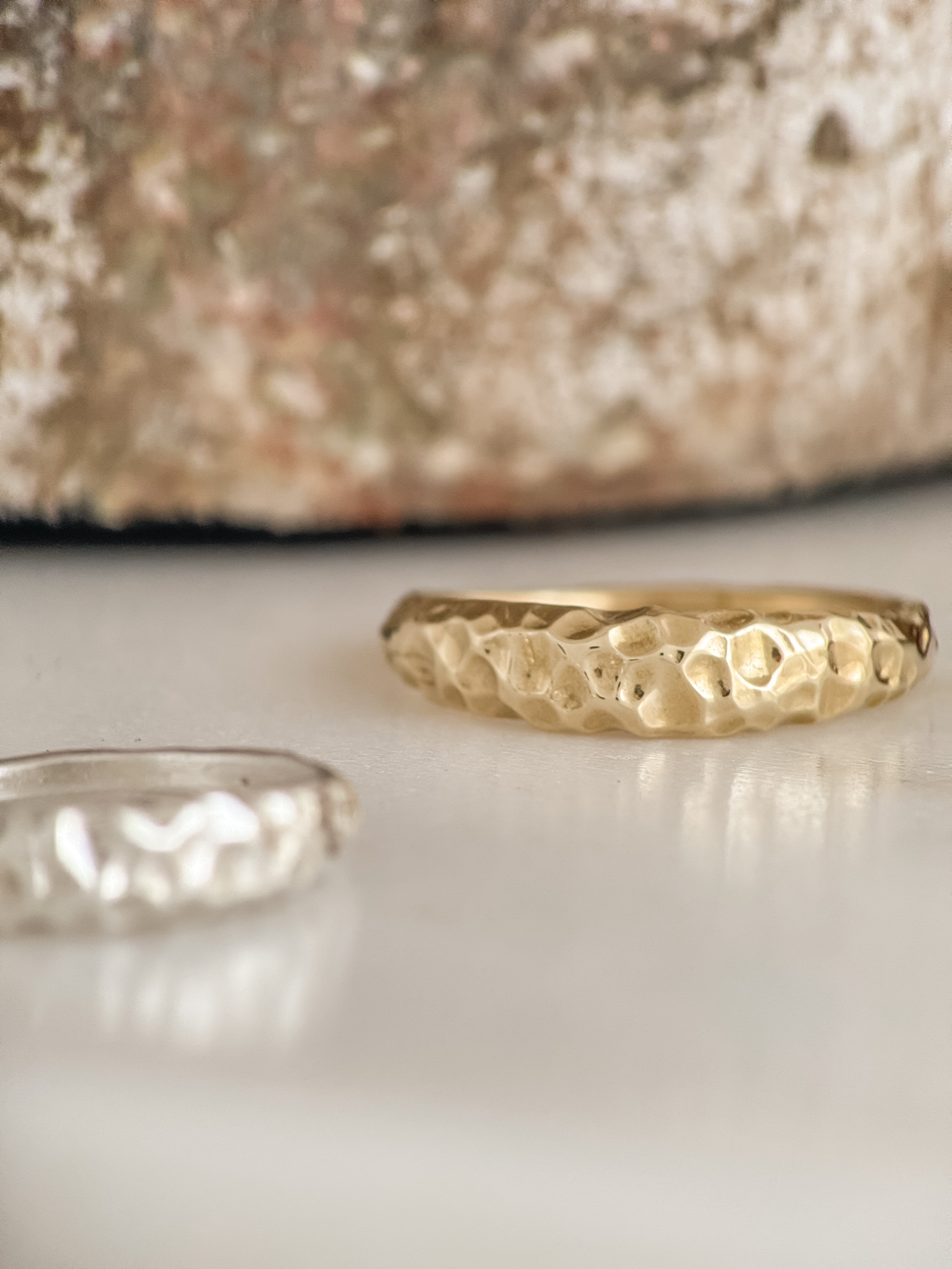 Two gold rings with textured surfaces on a reflective surface.