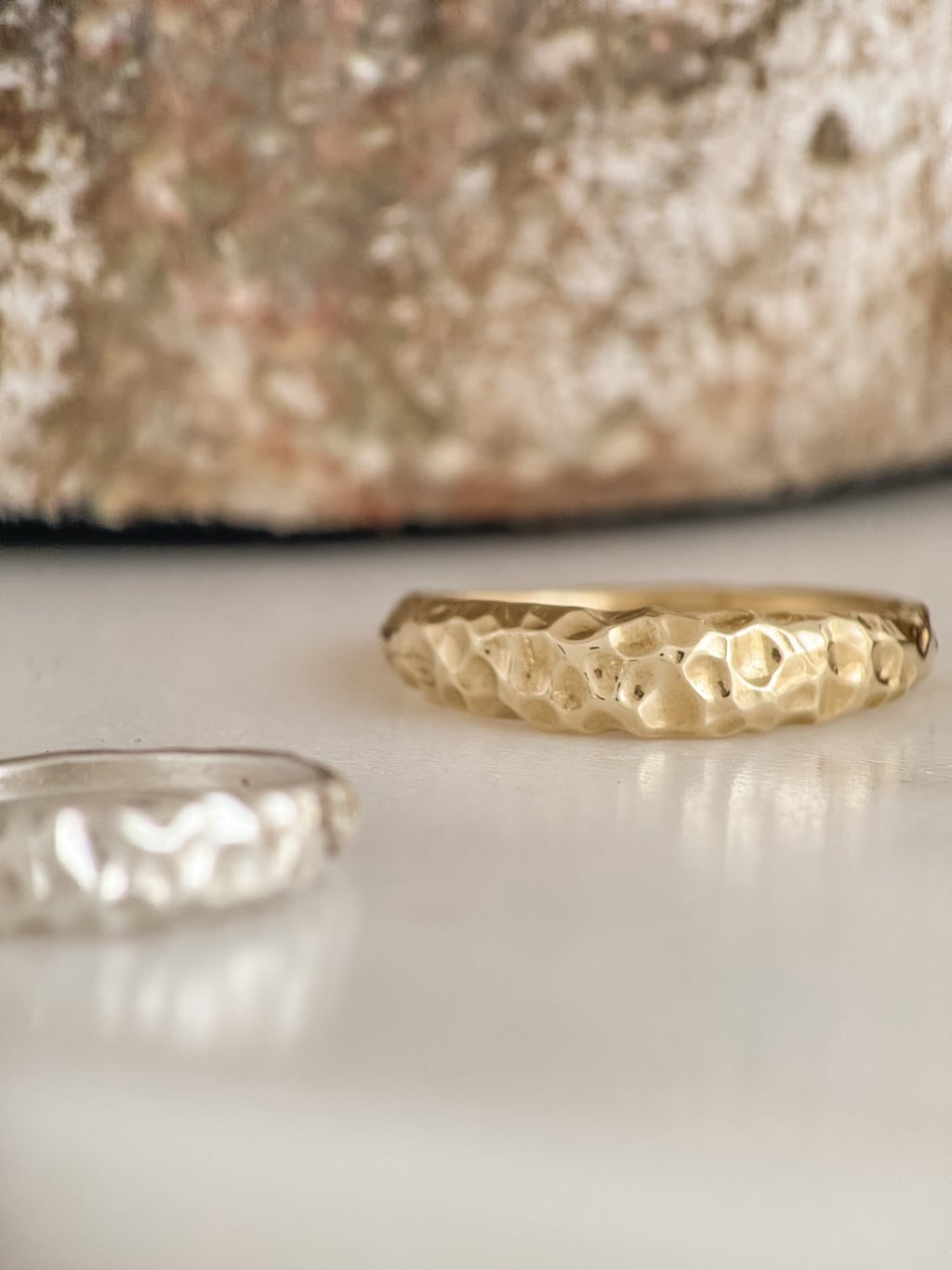 Two gold rings with textured surfaces on a reflective surface.