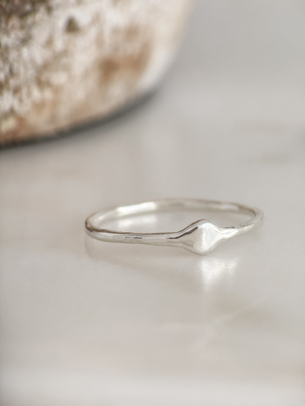 A delicate sterling silver ring with a small, organic wavy diamond-shaped accent on the band, resting on a light marble surface.