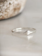 A delicate sterling silver ring with a small, organic wavy diamond-shaped accent on the band, resting on a light marble surface.