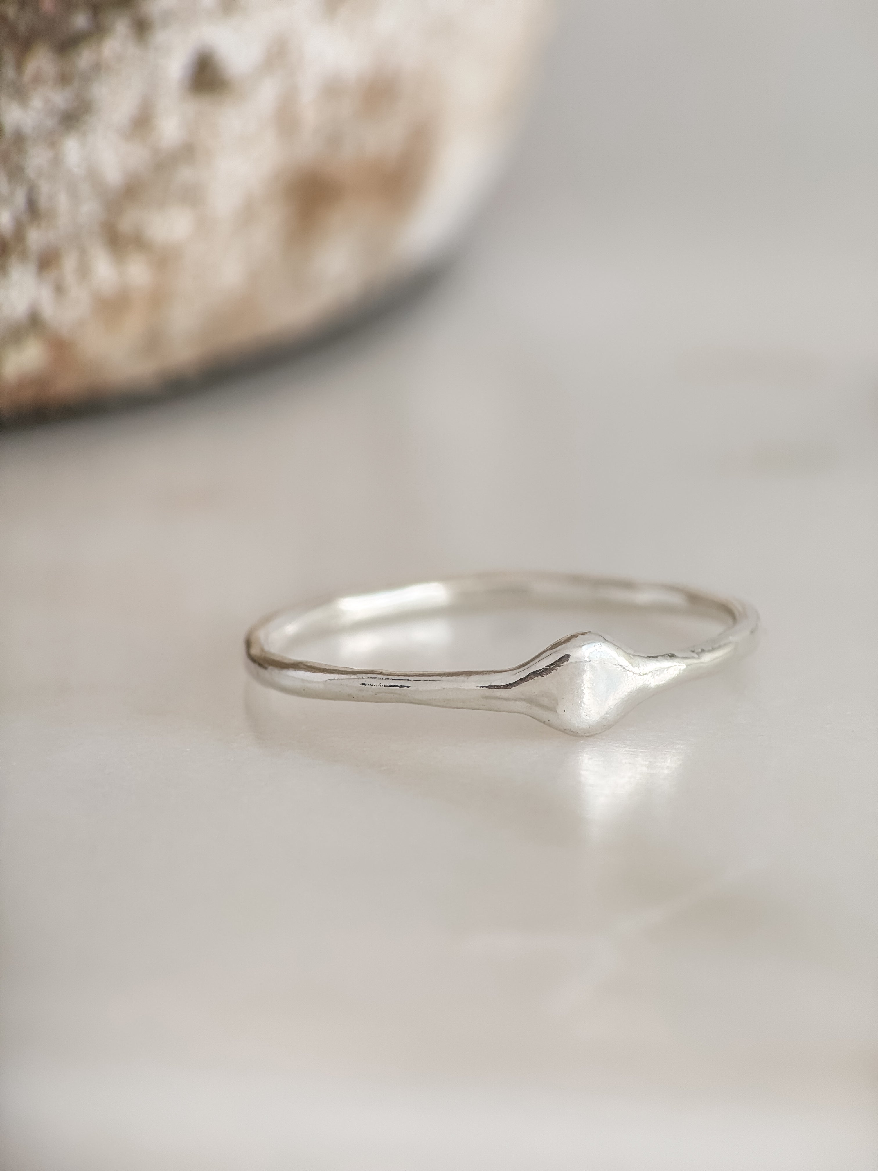 A delicate sterling silver ring with a small, organic wavy diamond-shaped accent on the band, resting on a light marble surface.