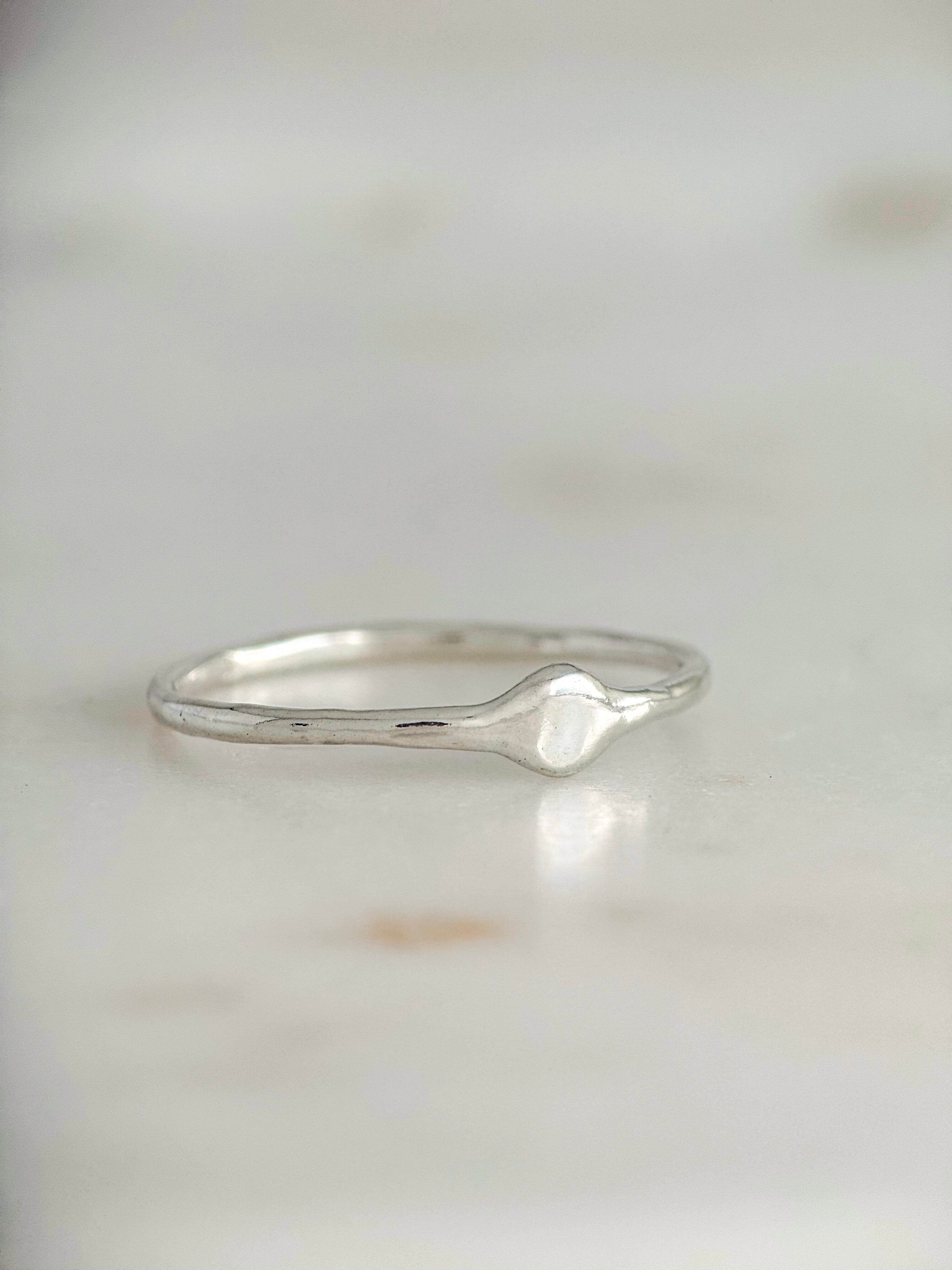 A delicate sterling silver ring with a small, organic-shaped raised center, resting on a light marble surface.