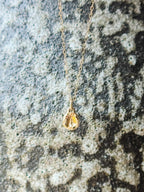 A delicate gold chain necklace with a small molten initial texture, resting on a textured gray and white stone surface.