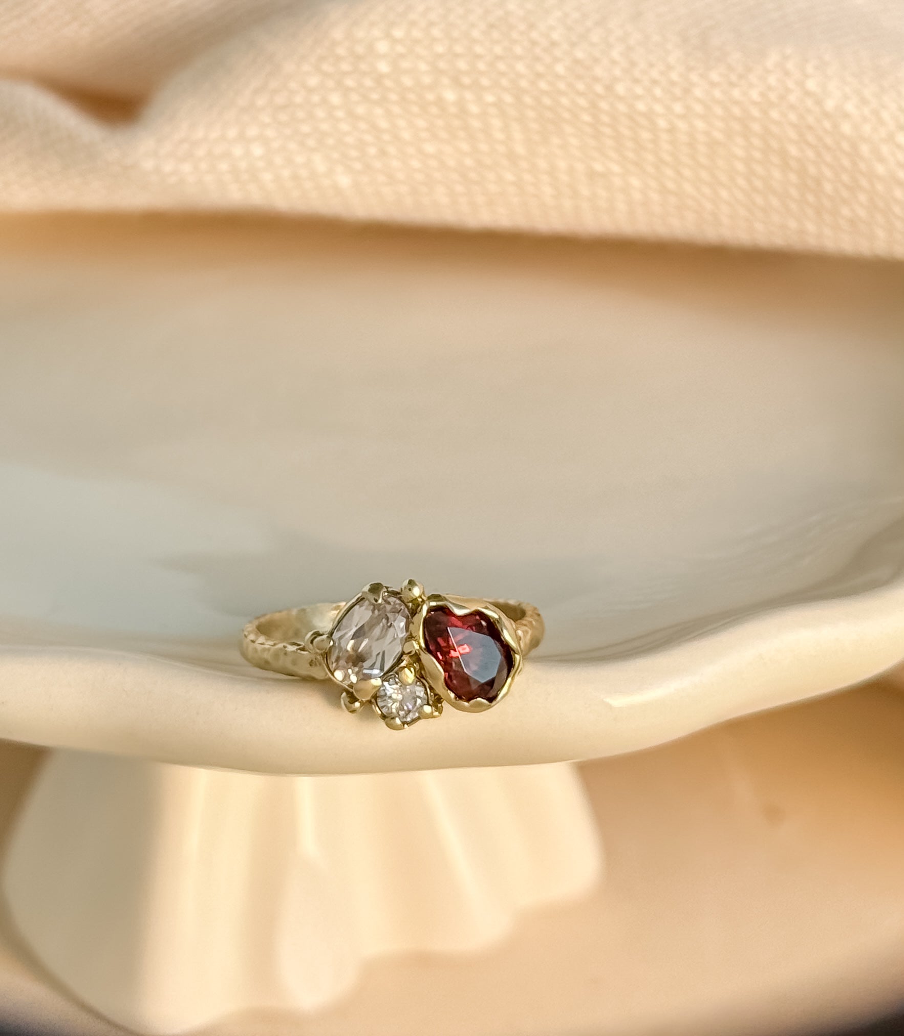Gold cluster ring with three gemstones on a beige fabric background