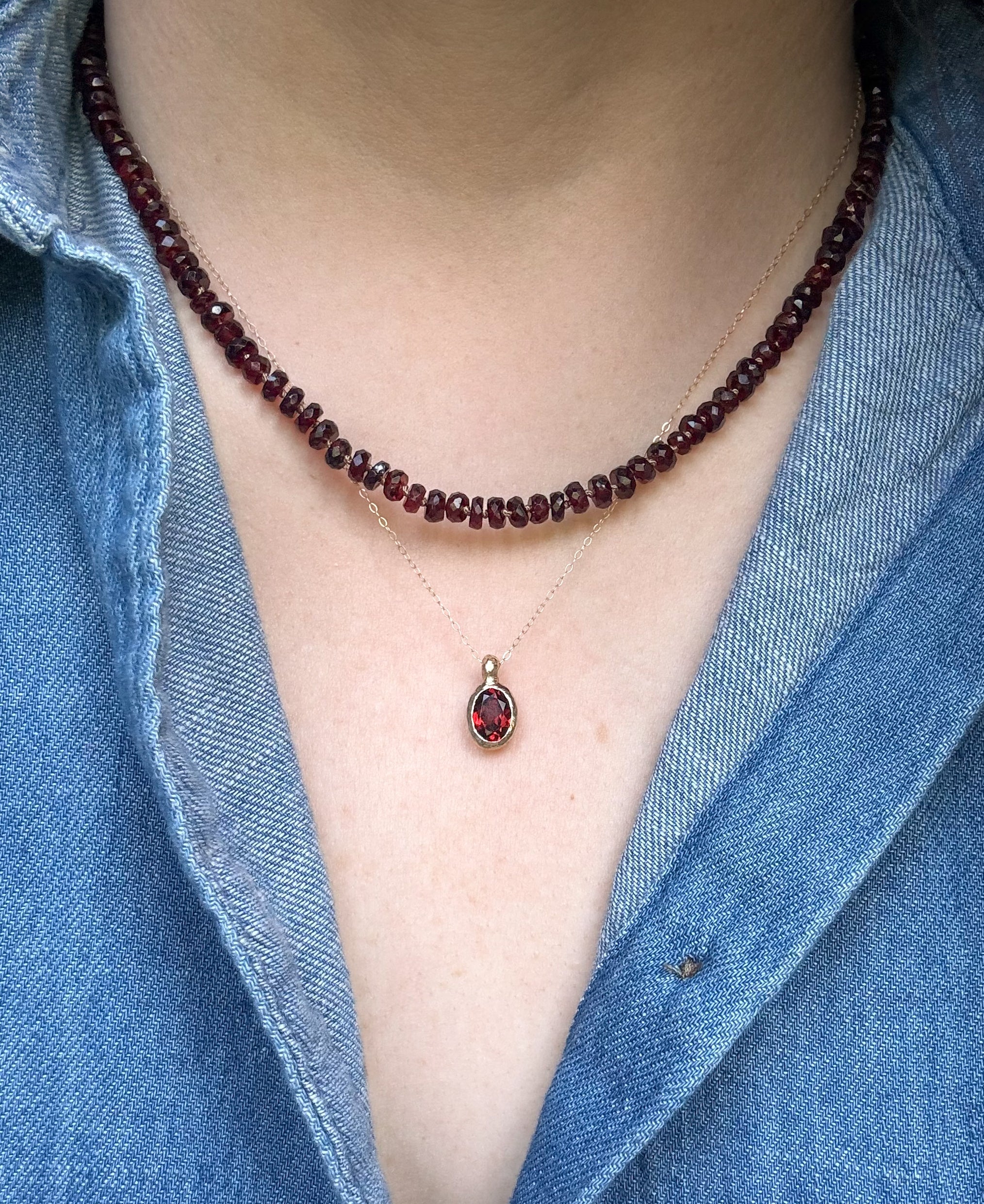 Garnet beaded necklace layered with a garnet pendant necklace worn by a person wearing a blue denim shirt.