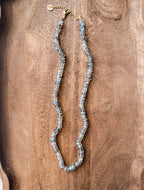 Labradorite gemstone beaded necklace, knotted in silk, with gold fill findings. Necklace laying on dark wood background.