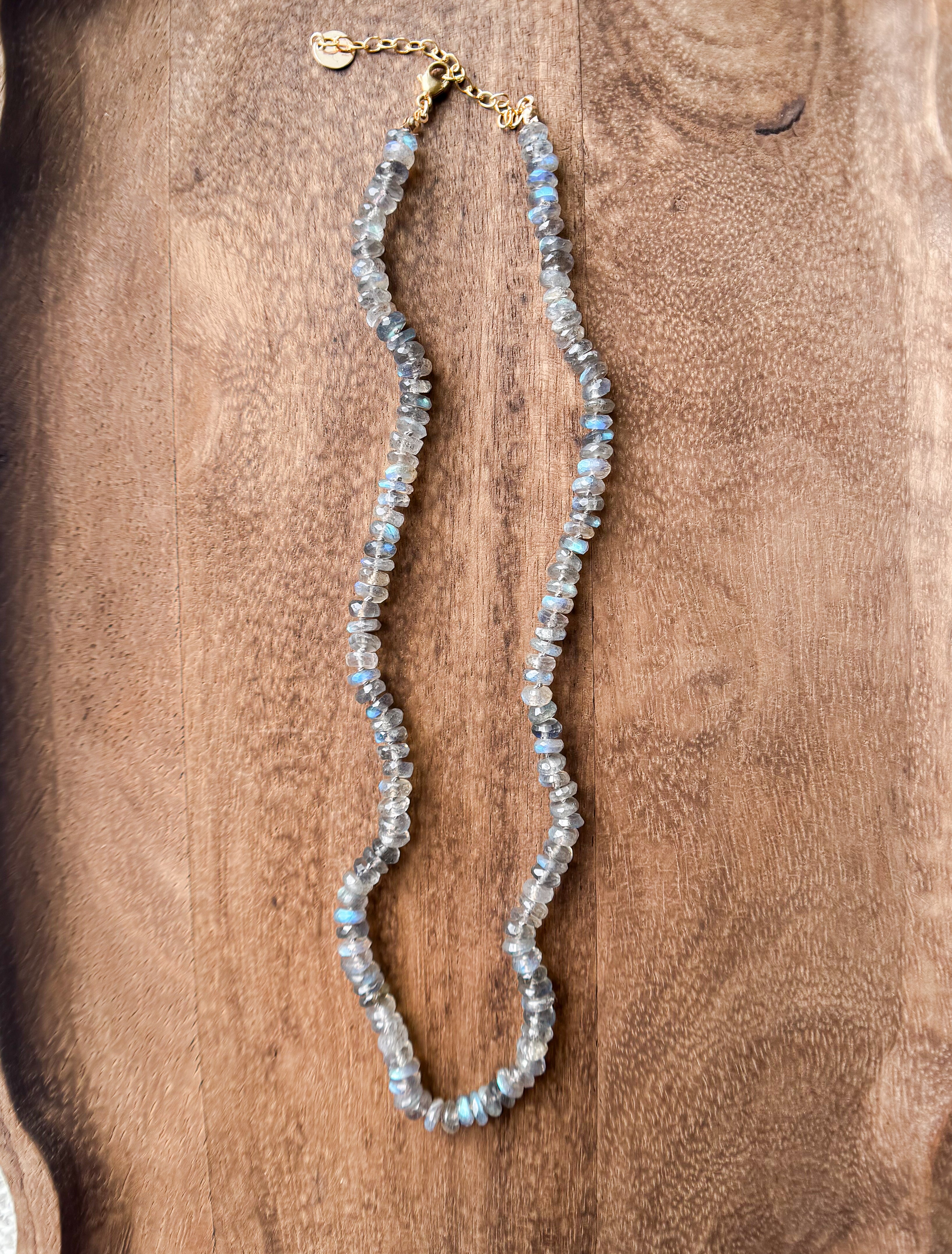Labradorite gemstone beaded necklace, knotted in silk, with gold fill findings. Necklace laying on dark wood background.