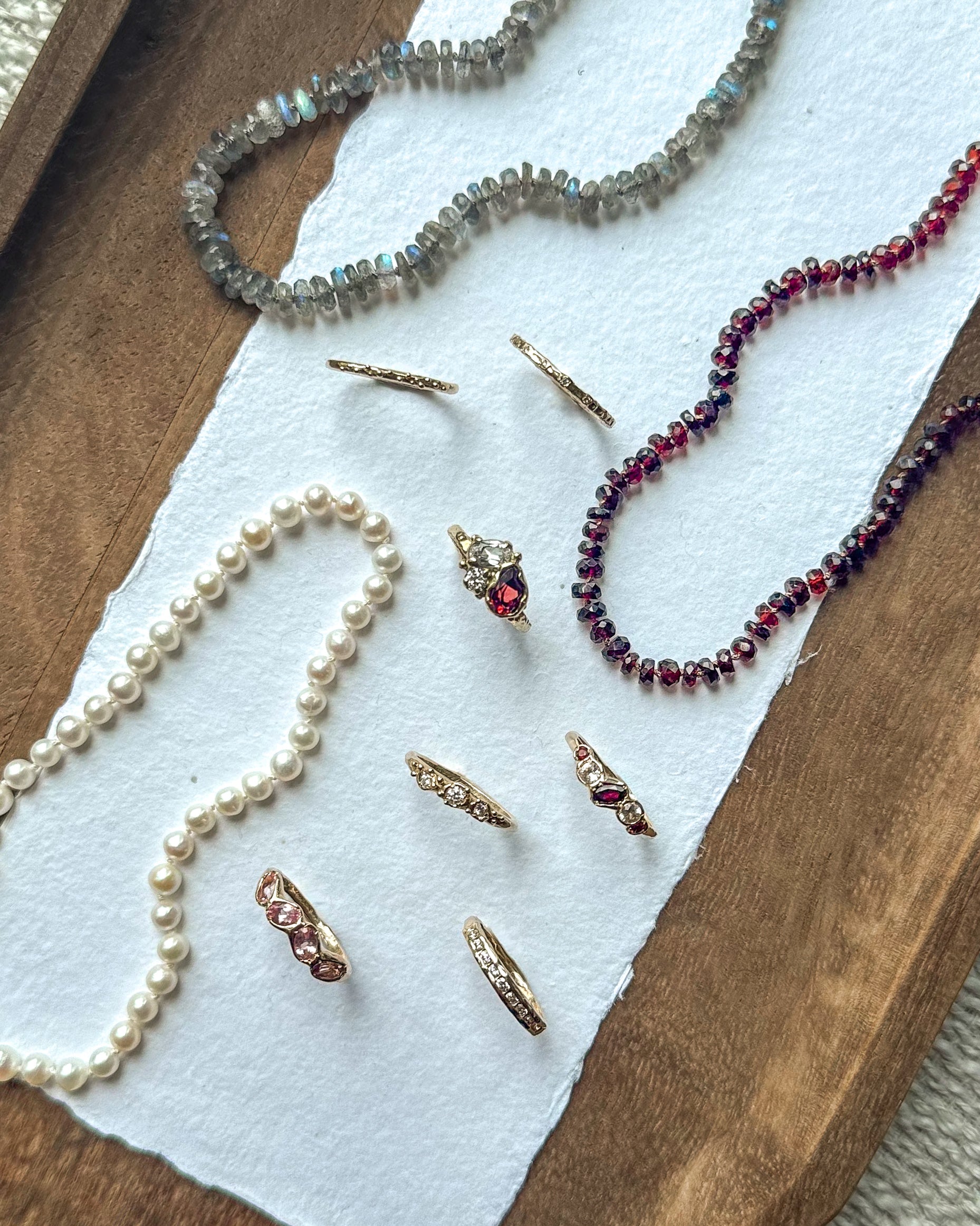 Jewelry including necklaces and earrings on a wooden surface with white paper underneath.