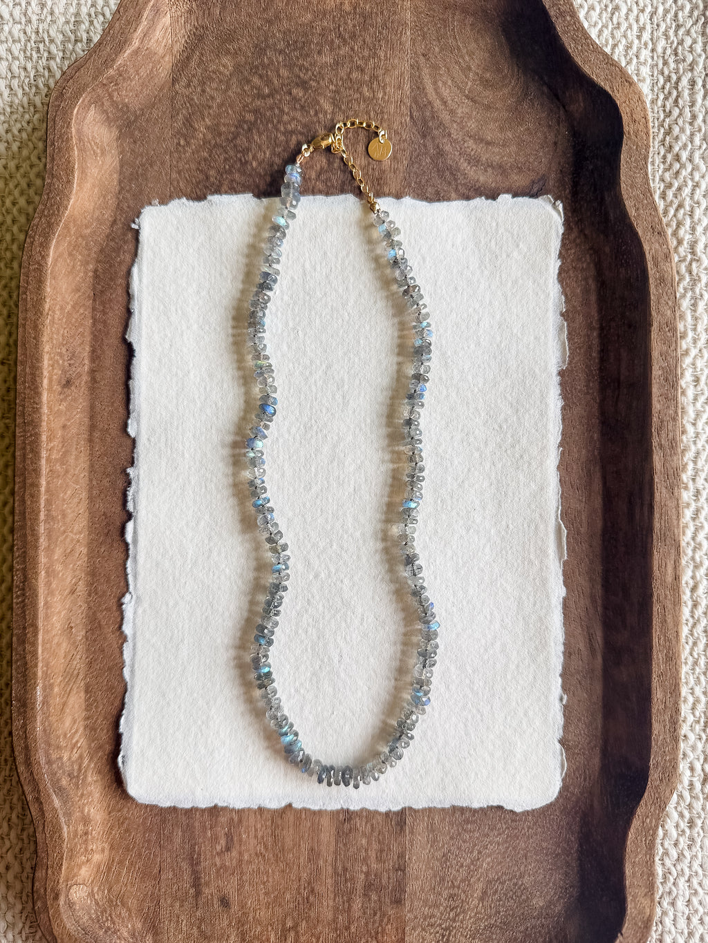 Necklace with labradorite beads on a white card, placed on a wooden tray.