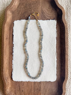 Necklace with labradorite beads on a white card, placed on a wooden tray.