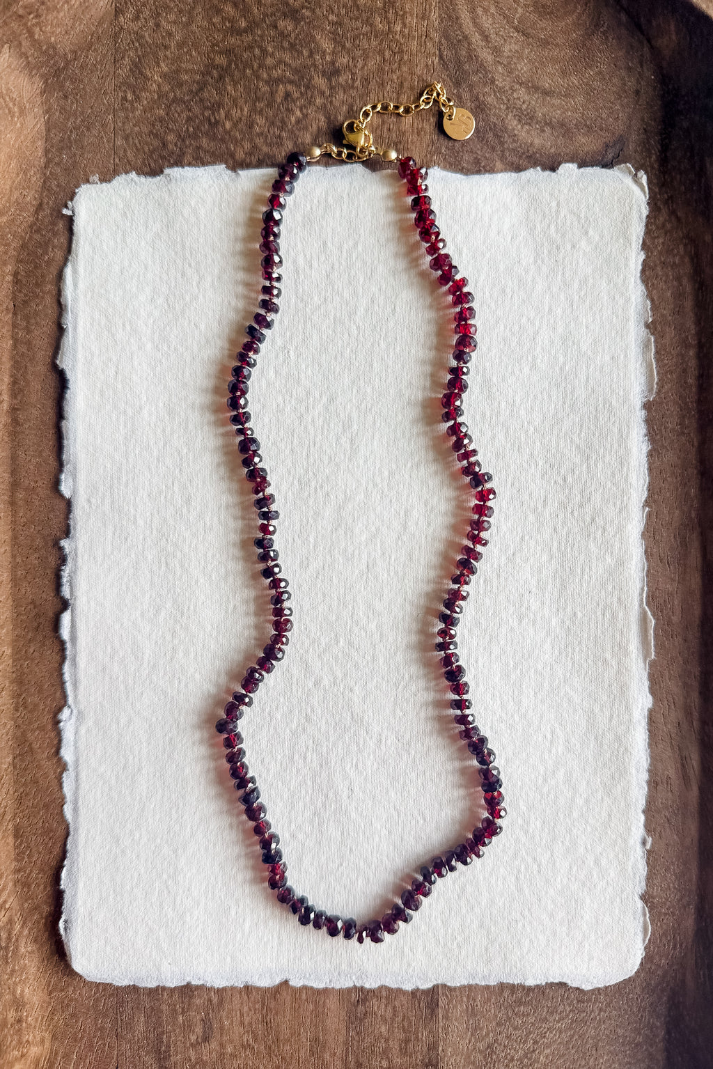 Necklace with red beads on a white textured paper against a wooden background