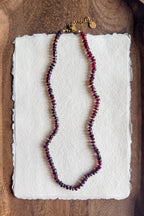Necklace with red beads on a white textured paper against a wooden background