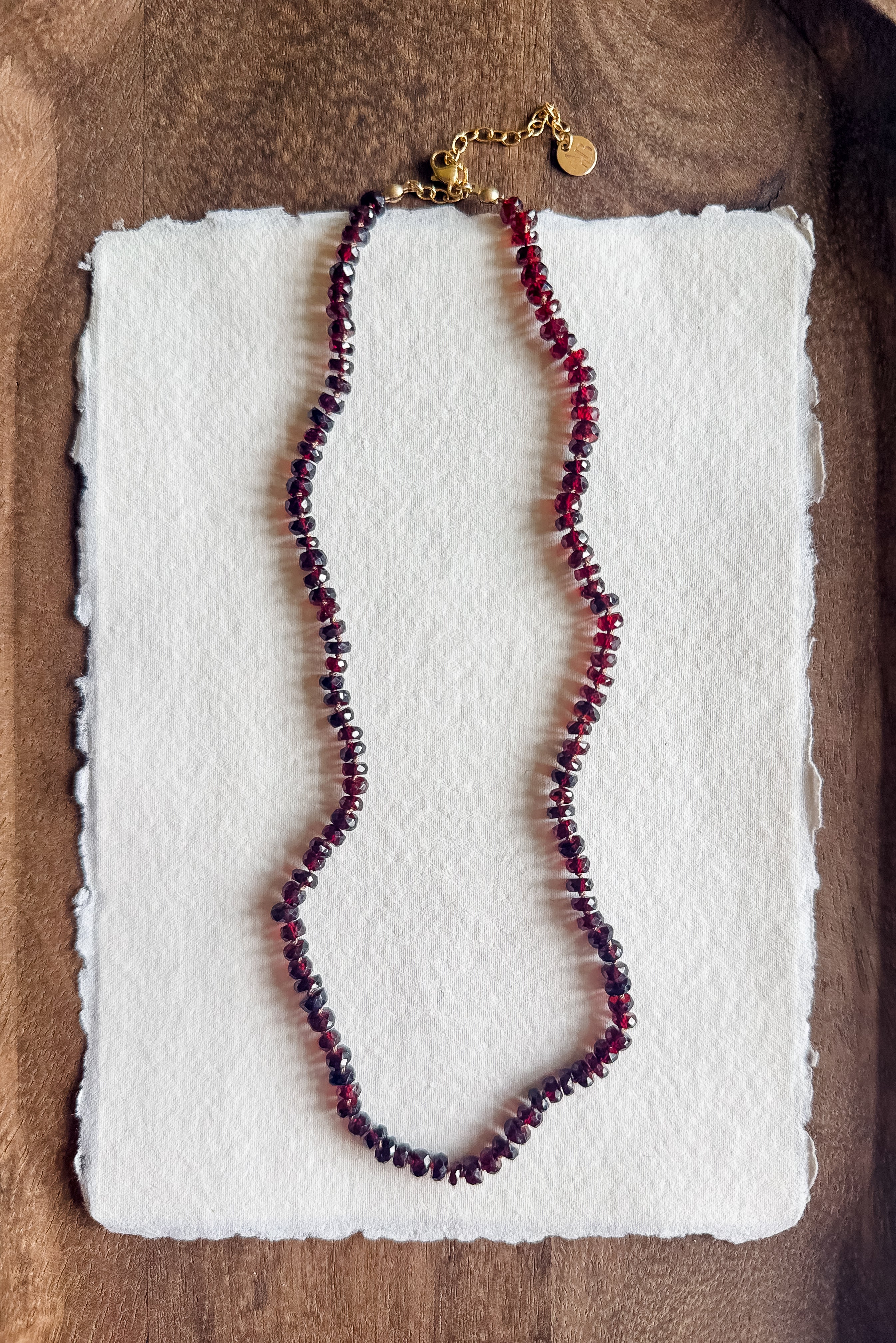 Necklace with red beads on a white textured paper against a wooden background