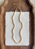 Pearl necklace on a white card with a wooden tray background