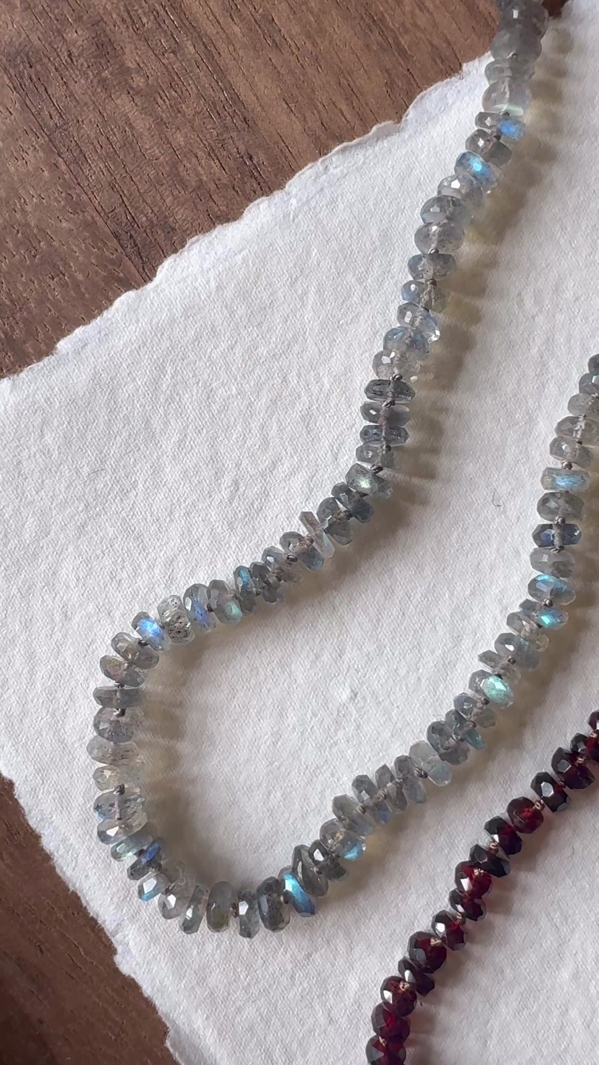 A video panning across three knotted silk gemstone bead necklaces. Labradorite, Garnet, and Pearl.